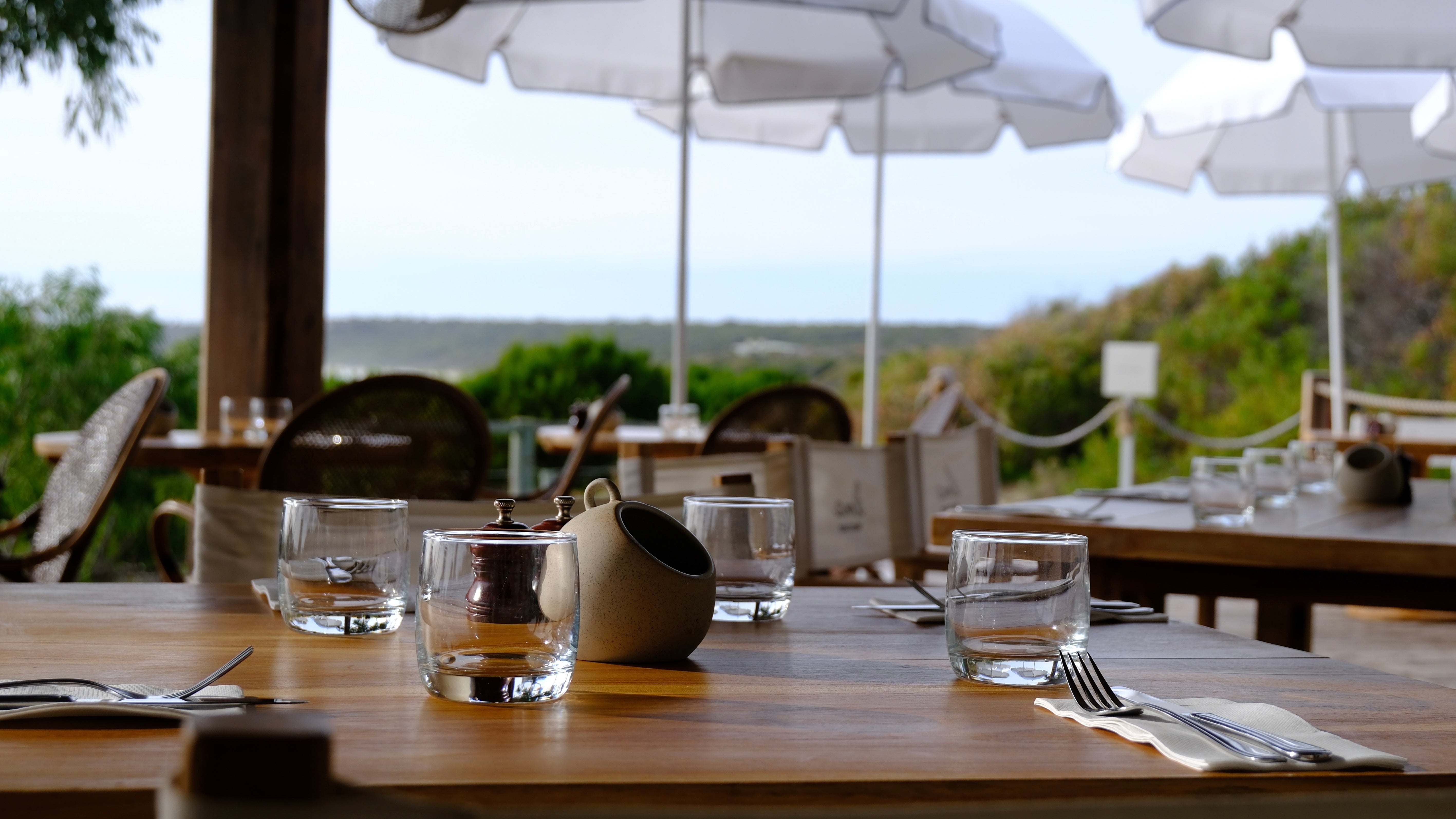 Outdoor dining setup with tables, chairs, and umbrellas in a scenic location.