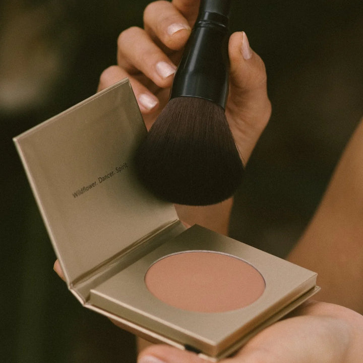 Makeup blush compact with a brush held above it