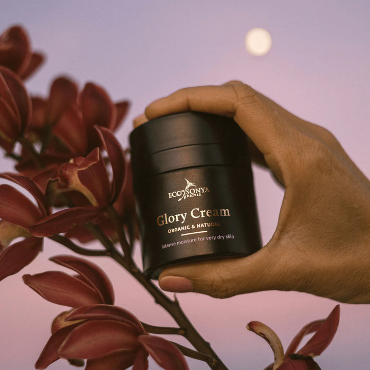 Hand holding a jar of Eco Tan Glory Cream with flowers and moon in the background