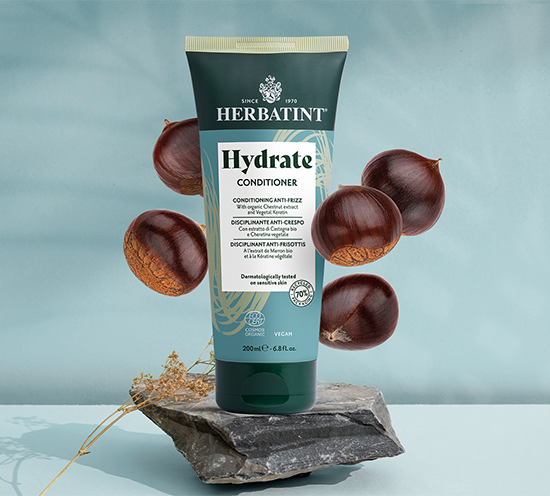 Herbatint Hydrate Conditioner tube with chestnuts on a stone surface against a light blue background