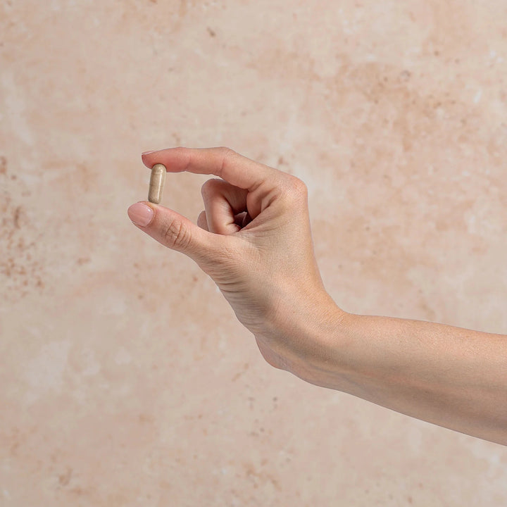 Hand holding a small cylindrical object against a beige background