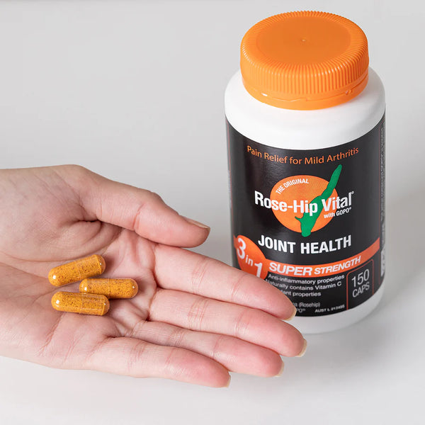 Hand holding capsules next to a bottle of Rose-Hip Vital Joint Health supplement.