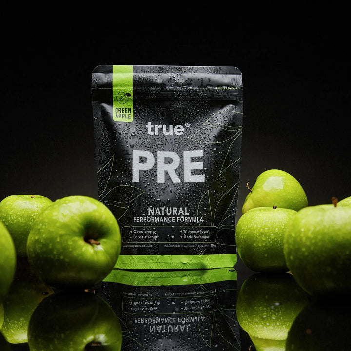 Black supplement package labeled 'true PRE' surrounded by green apples on a reflective surface with a black background