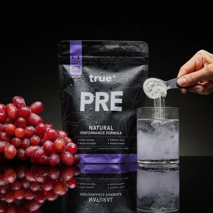 True Pre supplement package with grapes and a glass of water on a dark background