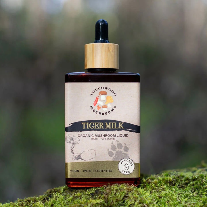 Bottle of Tiger Milk organic mushroom liquid on a mossy surface with a blurred natural background