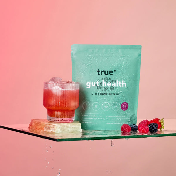 Teal 'true gut health' package with a glass of red drink and berries on a pink background
