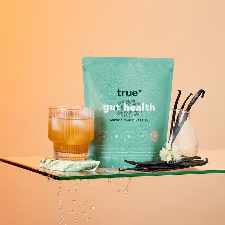 true gut health product packaging with a glass of tea and vanilla beans on a wooden board.