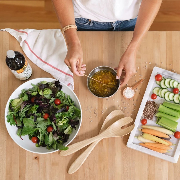 Person preparing a salad with various ingredients on a wooden table
